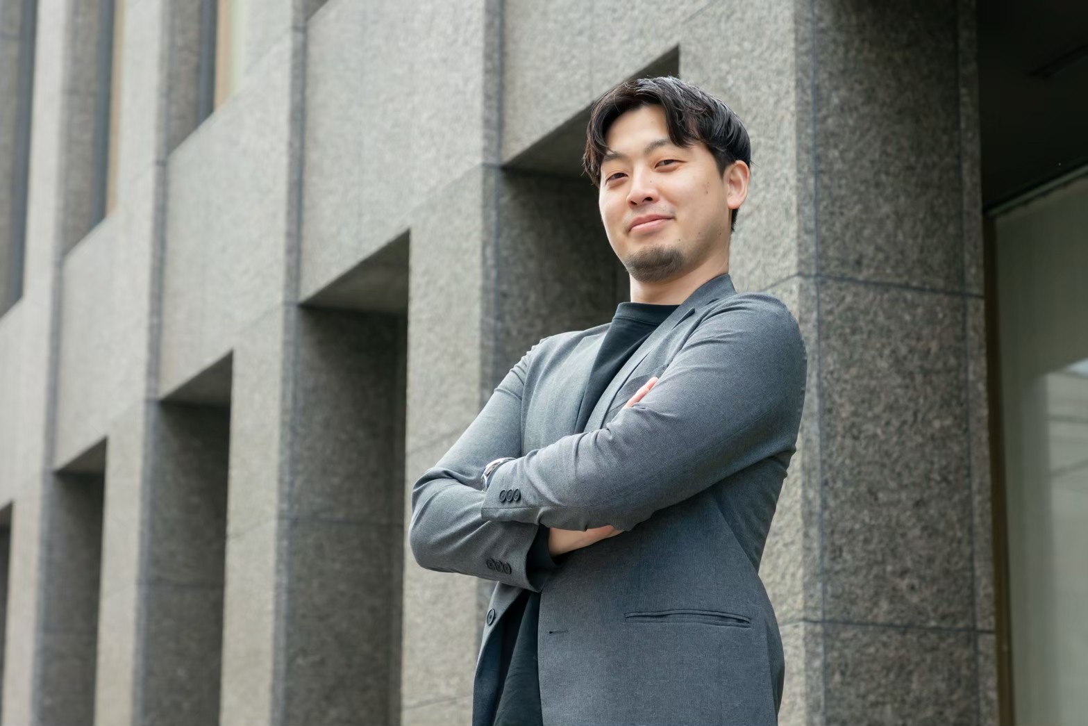 建物を背に自信ありげな表情で腕を組むBLAYN社員
